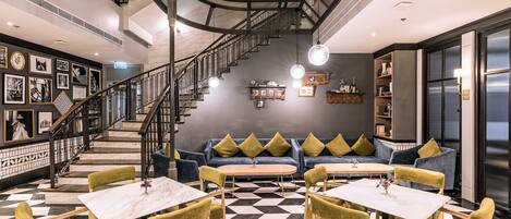 A modern interior with a checkered floor, a staircase, a sofa with cushions, and tables with chairs.