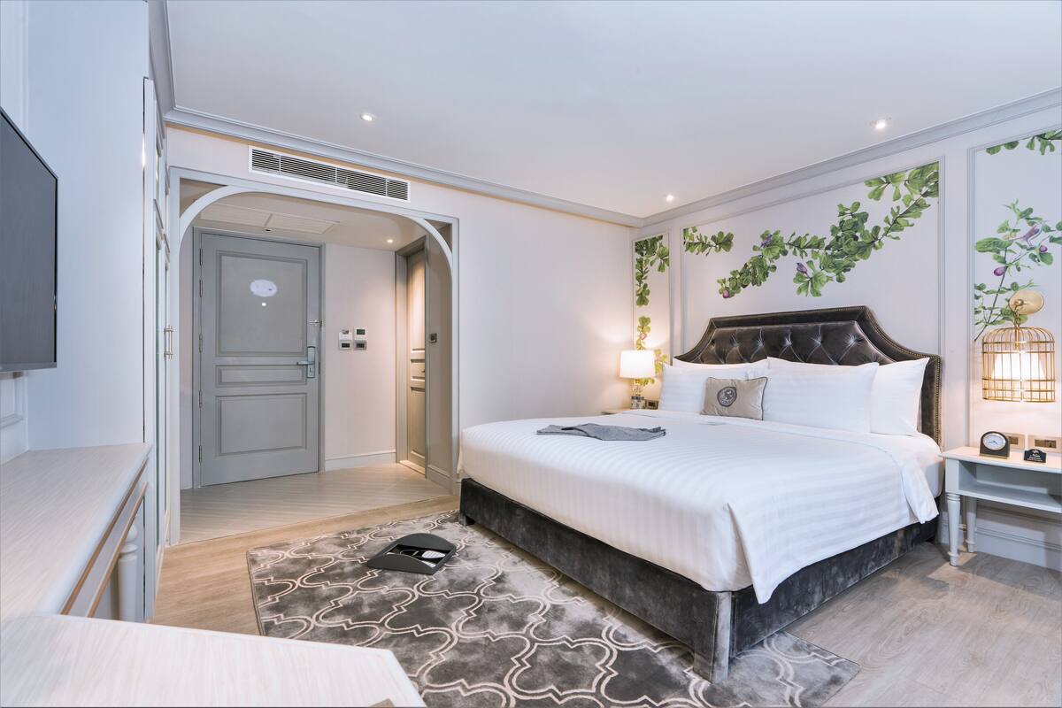 A modern hotel room with a large bed, a bedside table, a lamp, and a wall-mounted plant.