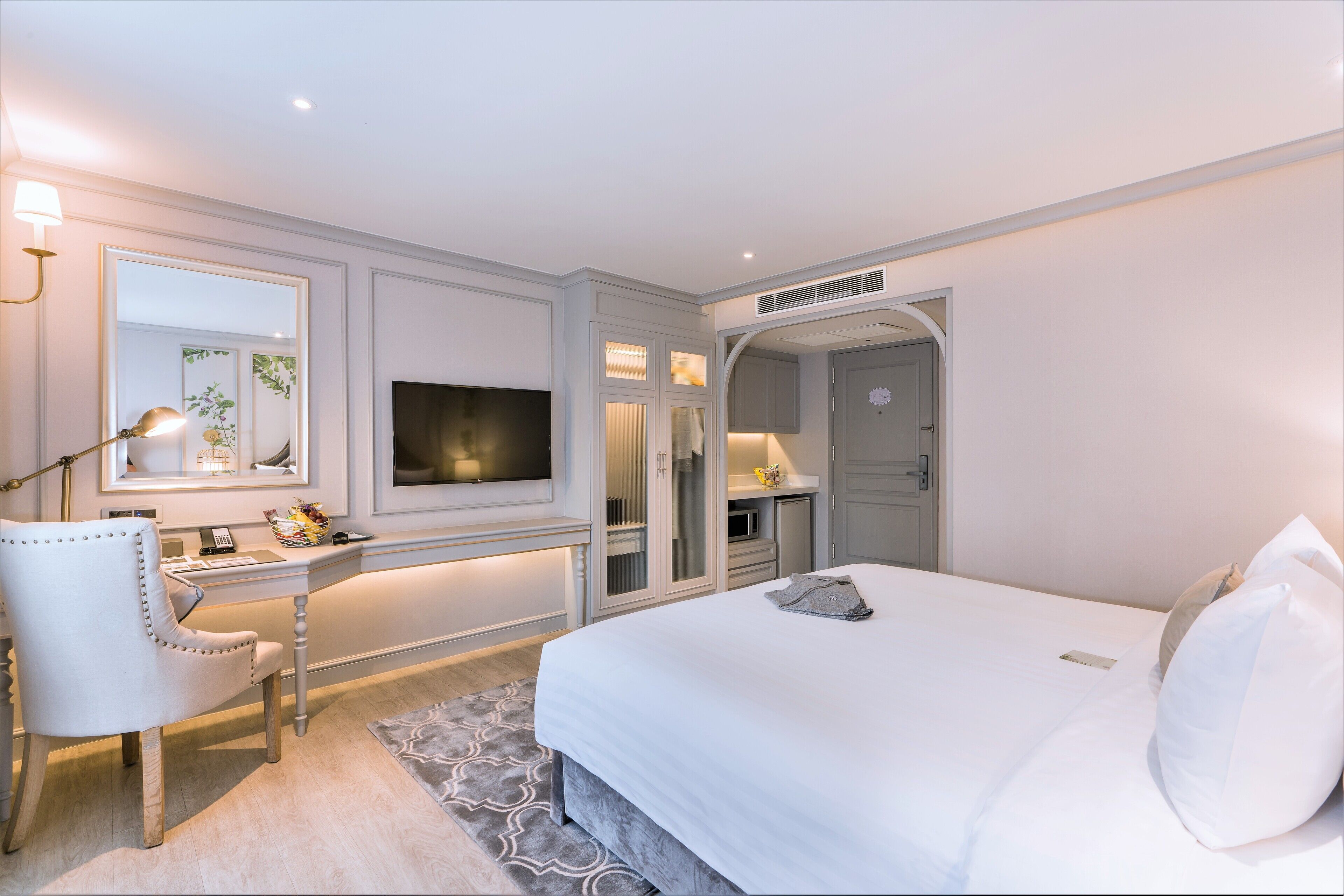 A modern hotel room with a large bed, a desk with a chair, a television, and a wardrobe.