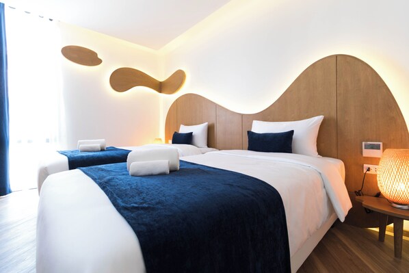 A modern hotel room with two beds, a wooden headboard, a bedside table with a lamp, and a wall-mounted light fixture. - Klub Hotel (Bangkok)