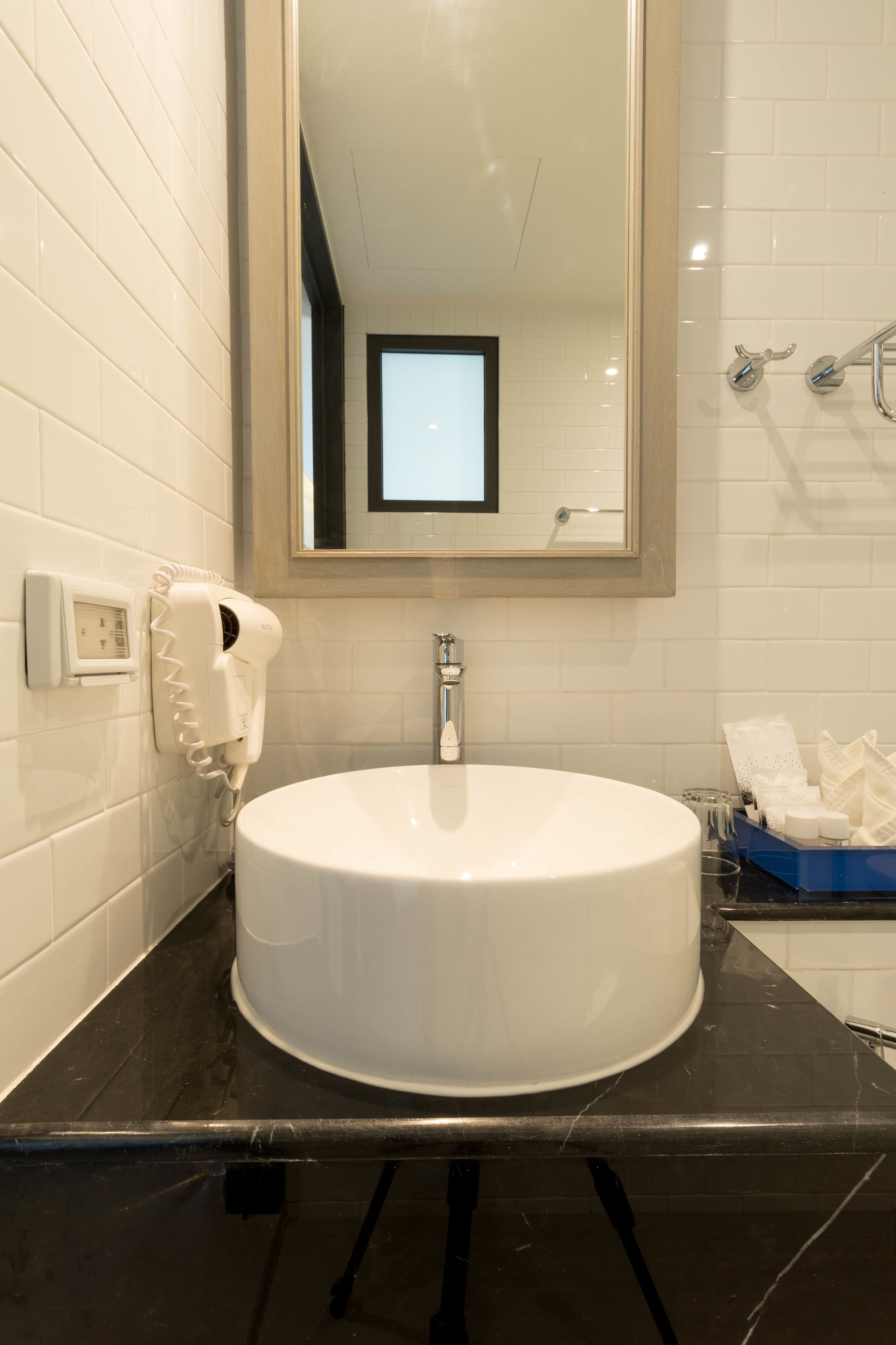 Une salle de bain avec un lavabo blanc, un miroir et un sèche-cheveux fixé au mur.