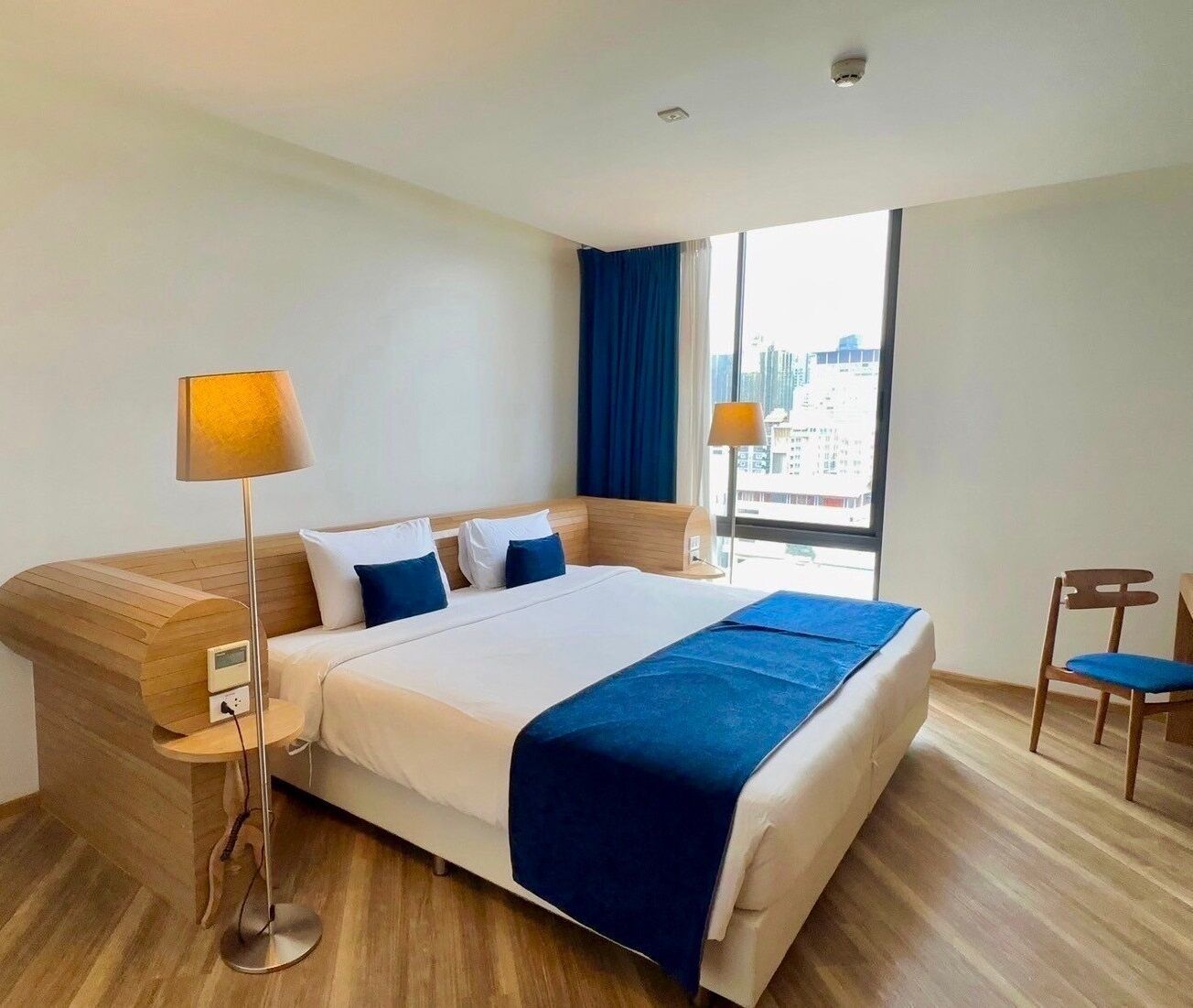 A modern hotel room with a large bed, a desk, a chair, and a view of the city.