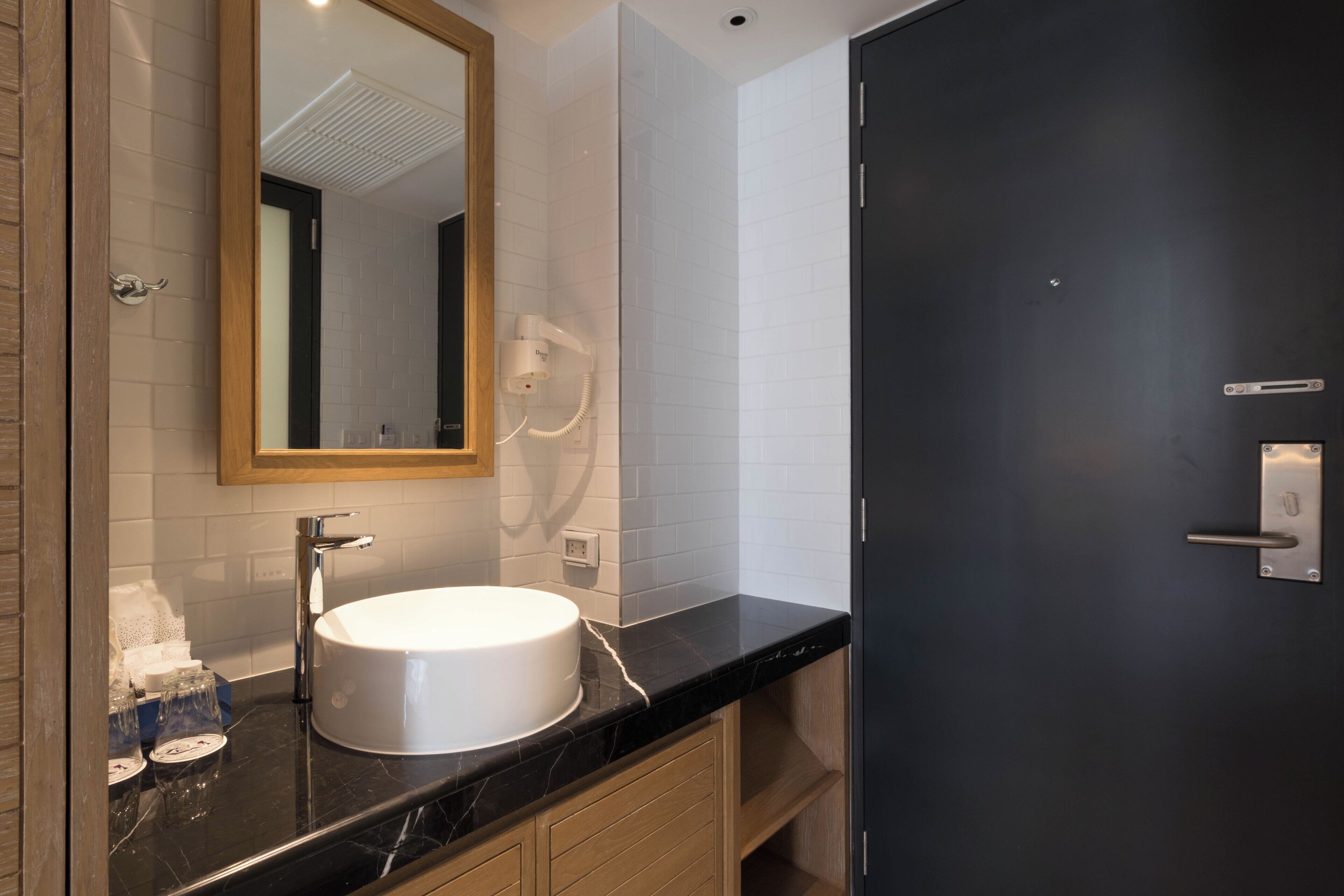 Une salle de bain moderne avec un lavabo blanc, un miroir et une porte sombre.