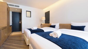 A hotel room with two beds, a wooden wardrobe, a bedside table with a lamp, and a door with a handle. - Klub Hotel (Bangkok)
