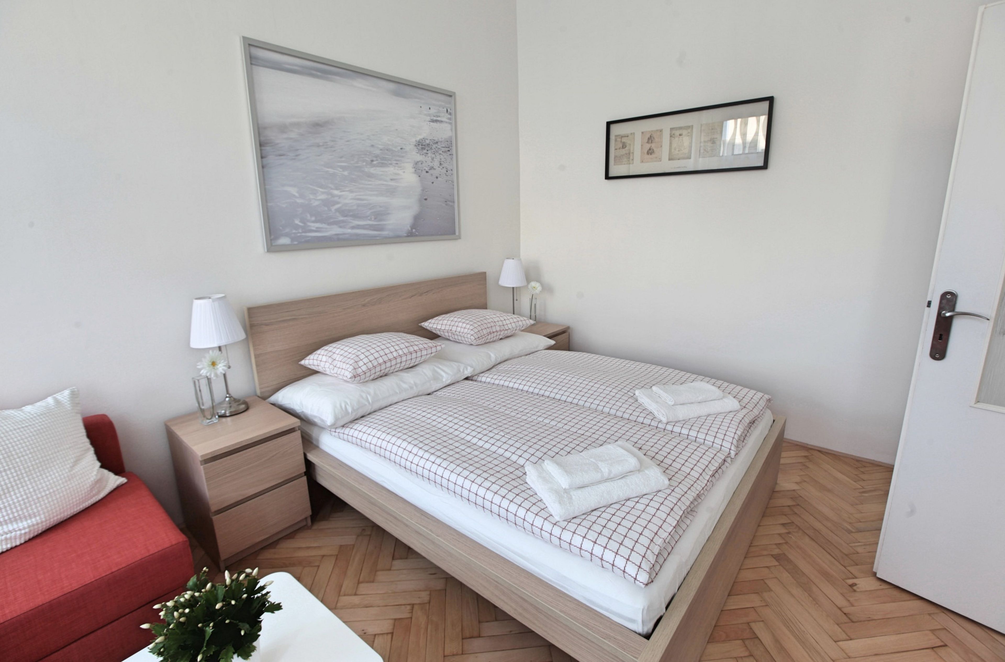 Un dormitorio ordenado con una cama, mesitas de noche, un sofá rojo y un cuadro colgado en la pared.