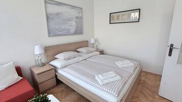 Un dormitorio ordenado con una cama, mesitas de noche, un sofá rojo y un cuadro colgado en la pared.