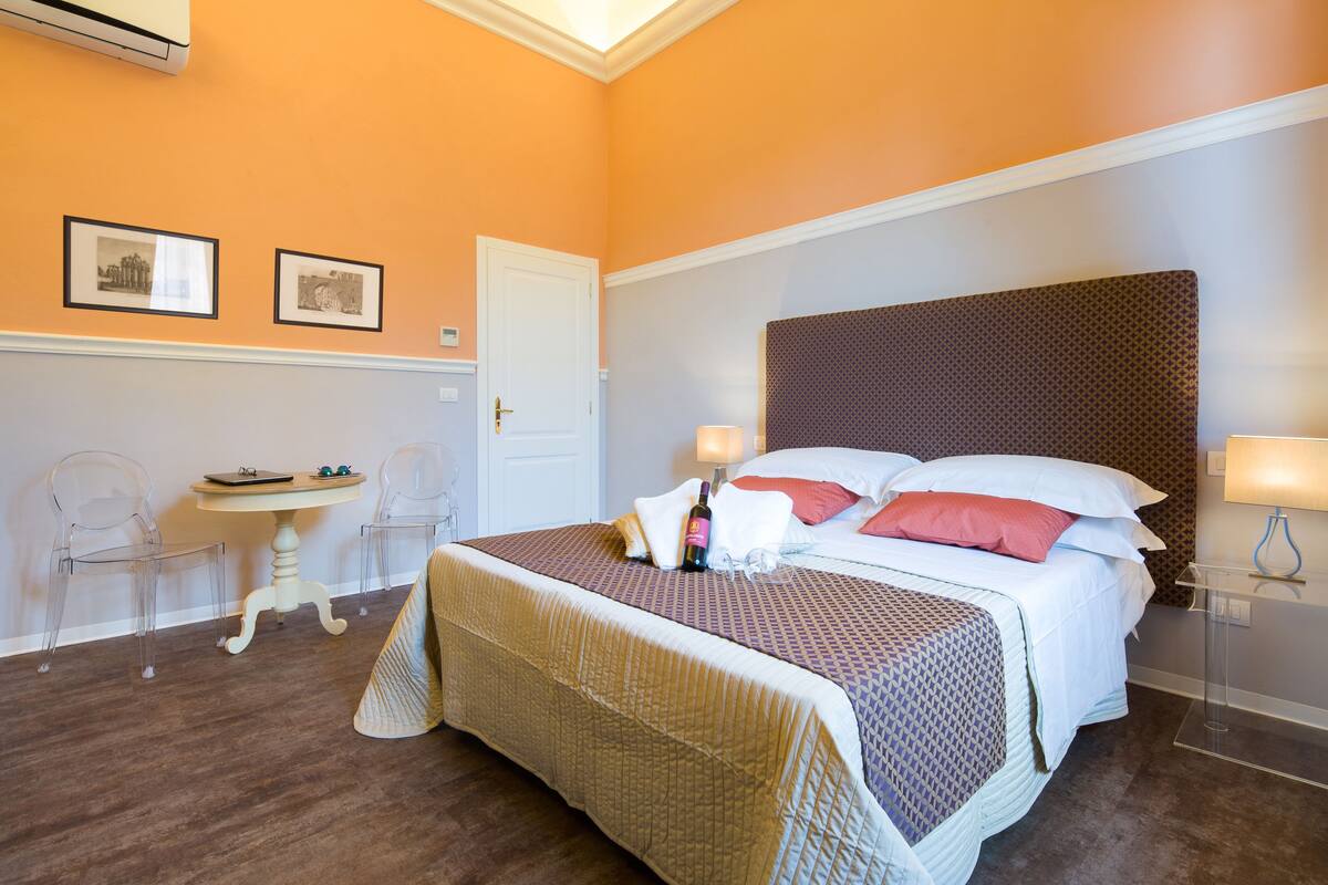 A hotel room with a large bed, two bedside tables, a small table with chairs, and framed pictures on the wall.