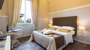 Een hotelkamer met een bed, bedlampen, een klein tafeltje met een stoel en een raam met gordijnen.