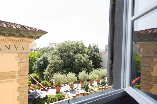 A view from a window overlooking a courtyard with potted plants and a building with "ANVS" on its facade. - B&B Residenza San Gallo 79 (Florence)