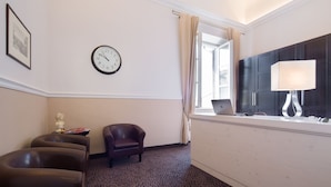 Een hotelkamer met een klok, een bureau met lamp, een stoel en een raam met gordijnen.