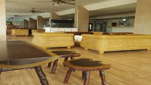 A spacious indoor area with wicker sofas, wooden tables, and ceiling fans. - Charming Inn Hotel (Pattaya)