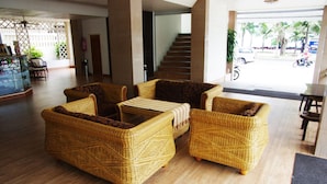 A lobby with wicker furniture, a staircase, and a view of the street outside. - Charming Inn Hotel (Pattaya)