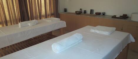 A room with two massage tables, each covered with a white sheet and a rolled towel.