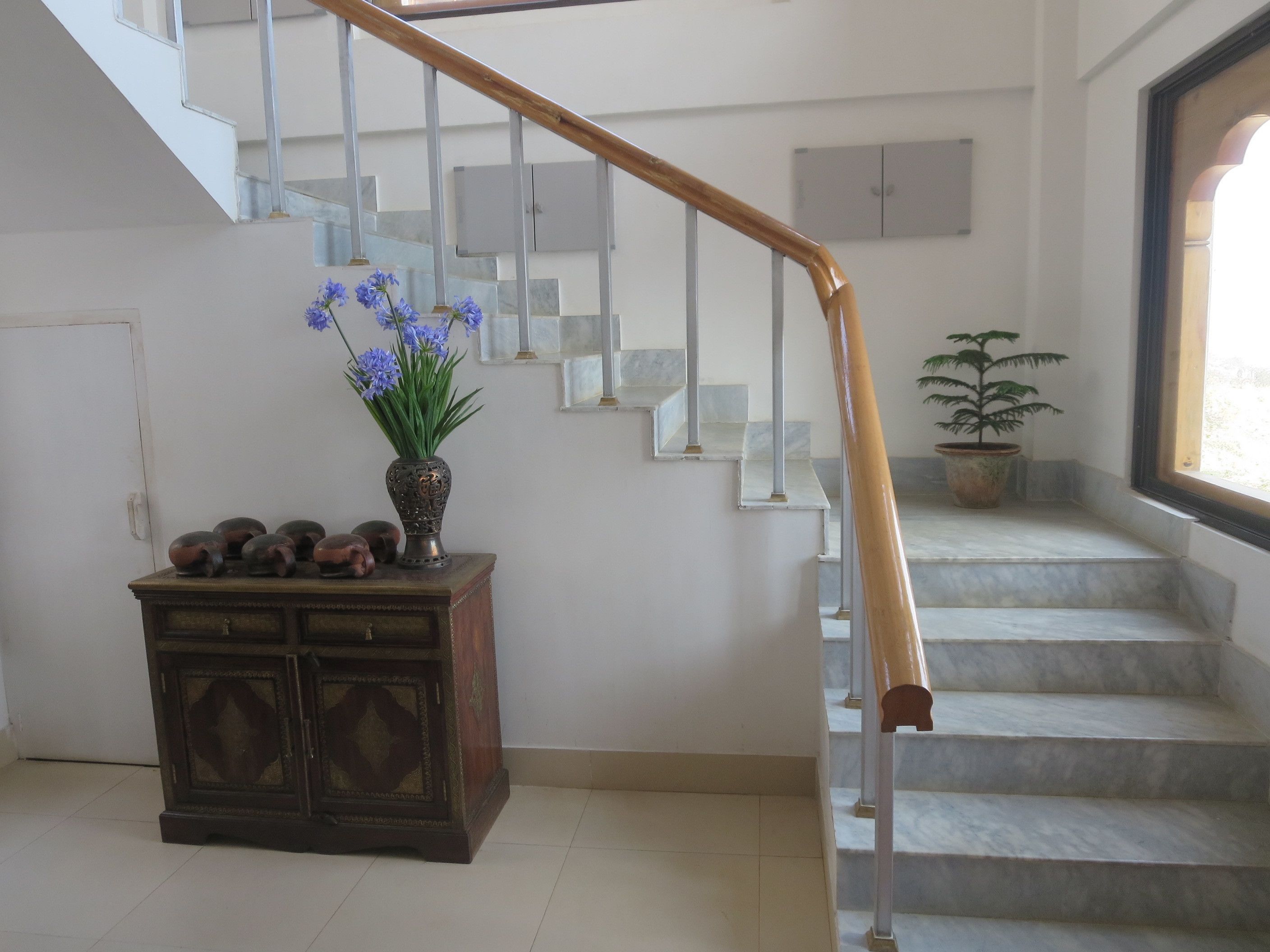 A staircase with a wooden handrail, a potted plant, and a decorative cabinet with vases.