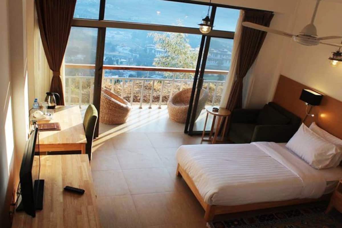 Ett hotellrum med en stor säng, ett skrivbord, en stol, ett litet bord och en balkong med flätade stolar.
