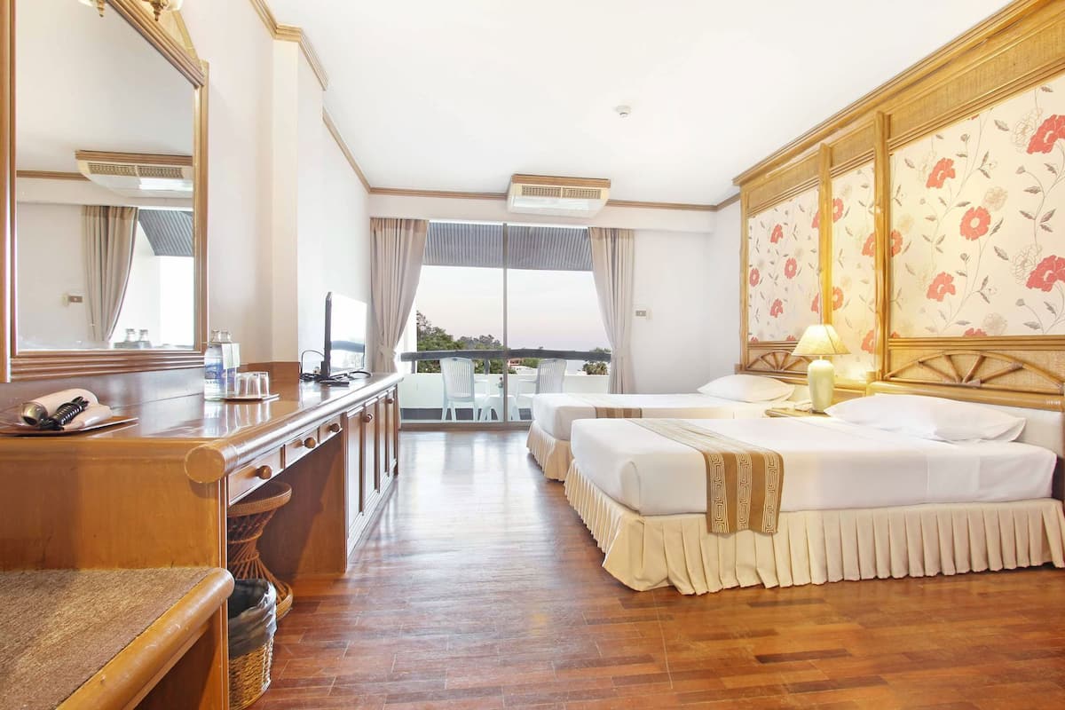 Habitación de hotel con un escritorio de madera, dos camas, un espejo grande y un balcón con vistas.