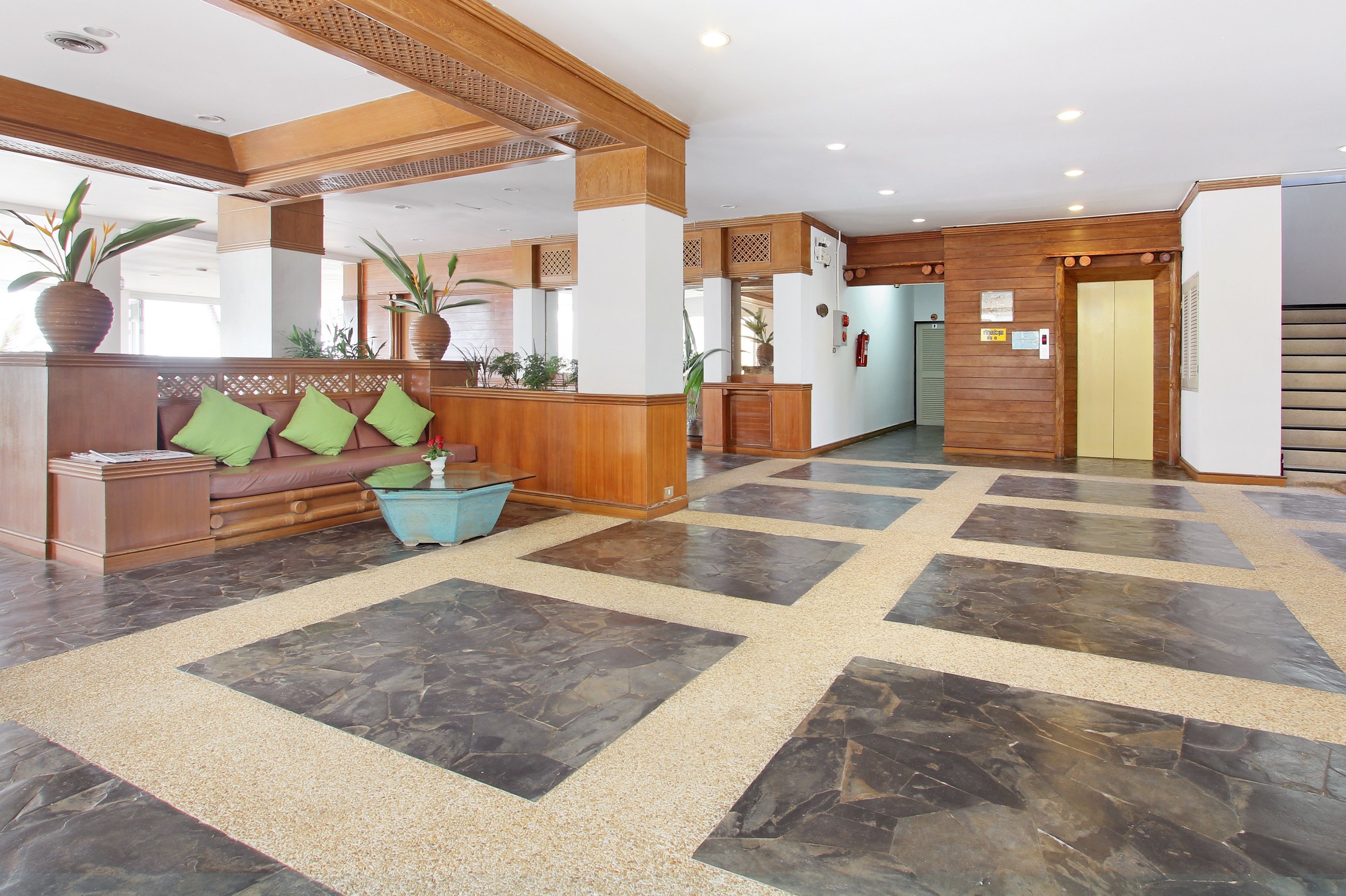 A lobby with a reception desk, a sofa with green cushions, and a large potted plant.