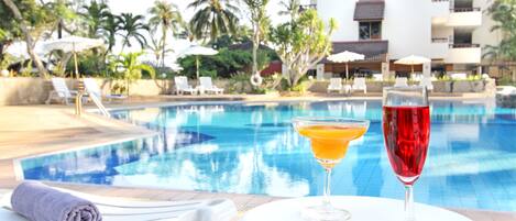 Vista de la piscina con sillas de descanso y una mesa con dos bebidas.