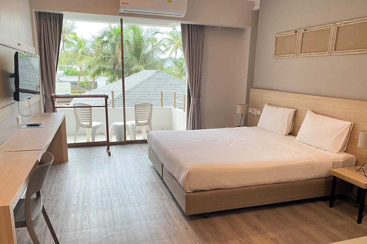 Habitación de hotel con cama, escritorio, silla y vistas a palmeras a través de la ventana.