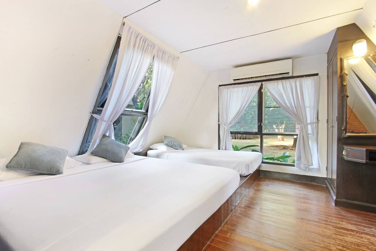 Una habitación con dos camas, una ventana con cortinas, un equipo de aire acondicionado y una escalera.
