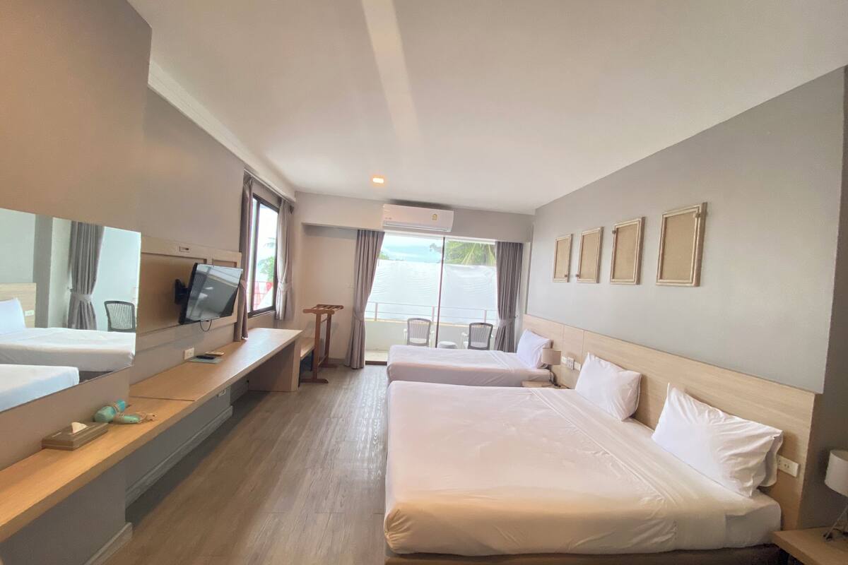 Habitación de hotel con dos camas, un escritorio con computadora, televisión y balcón con sillas.