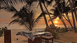 A table set for two with a floral tablecloth, two wooden chairs, and a view of the sunset over the ocean. - Rayong Chalet Resort (Klaeng)