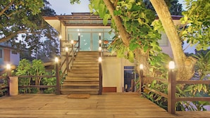 A wooden staircase leading to a building with a glass entrance, surrounded by trees and a wooden deck. - Rayong Chalet Resort (Klaeng)