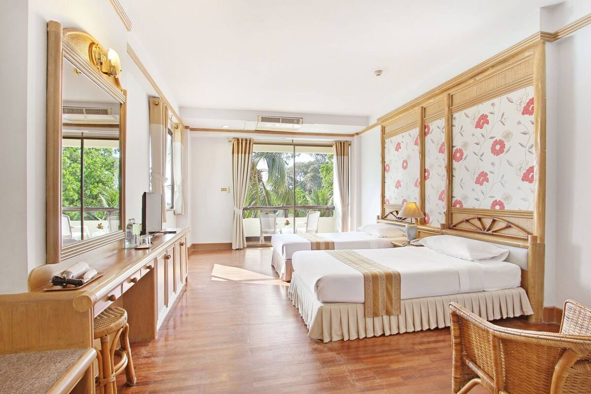 Habitación de hotel con dos camas, un escritorio, una silla y un amplio ventanal con vistas a zonas verdes.