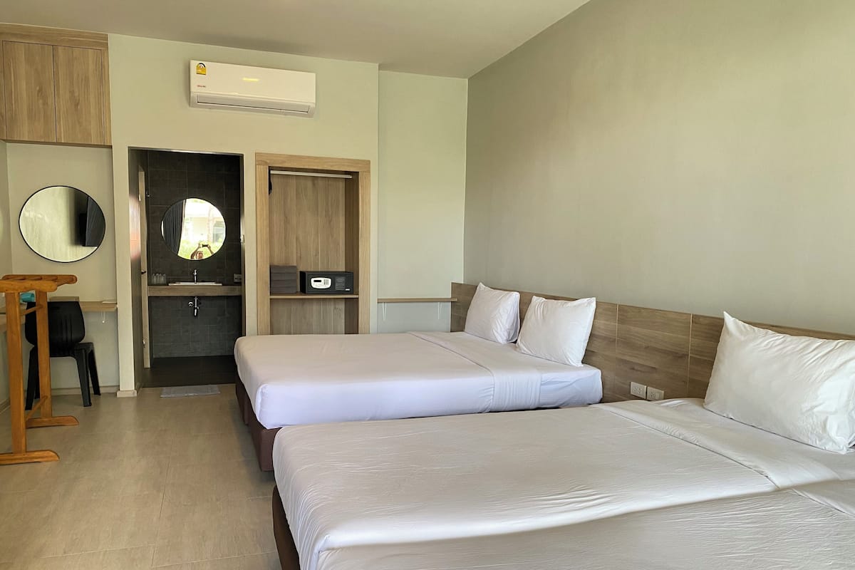 Habitación de hotel con dos camas, un armario de madera, un espejo, un lavamanos y un equipo de aire acondicionado.