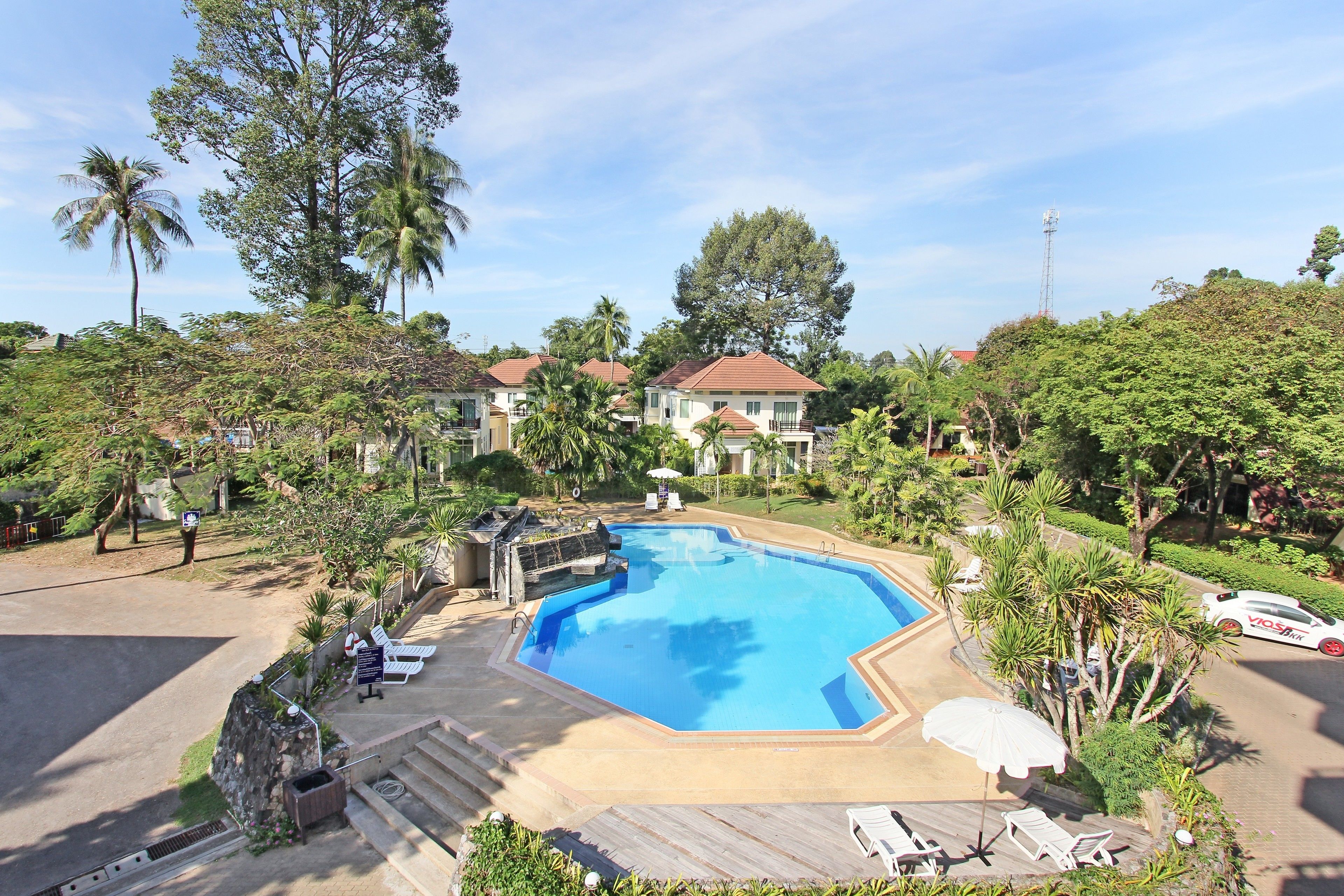 A swimming pool surrounded by lounge chairs and umbrellas, with a view of residential buildings in the background.