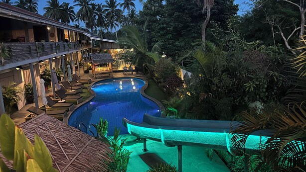A resort pool area with lounge chairs and umbrellas, surrounded by lush greenery and palm trees. - Samui Zenity Hotel (Koh Samui)