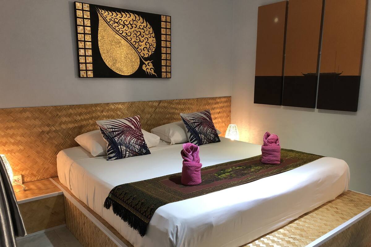 Una cama bien hecha con sábanas blancas, dos almohadas decorativas y un cabecero tejido.