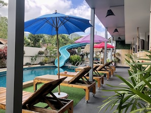 A pool area with lounge chairs and umbrellas, a water slide, and a thatched-roof structure. - Samui Zenity Hotel (Koh Samui)