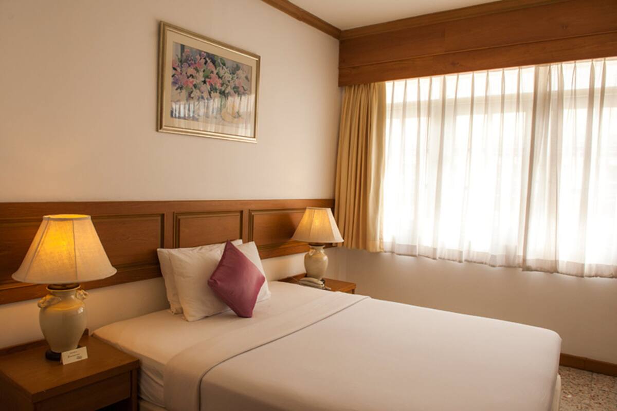 Une chambre d’hôtel avec un grand lit, deux lampes de chevet, une table de nuit, un tableau encadré au mur et une fenêtre avec des rideaux.