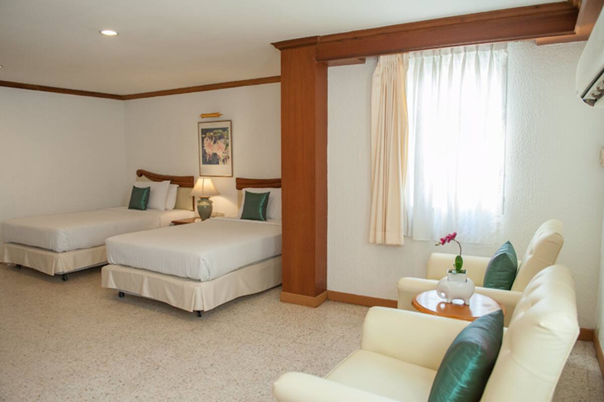Une chambre d’hôtel avec deux lits simples, un canapé, une petite table avec un vase et une fenêtre avec des rideaux.