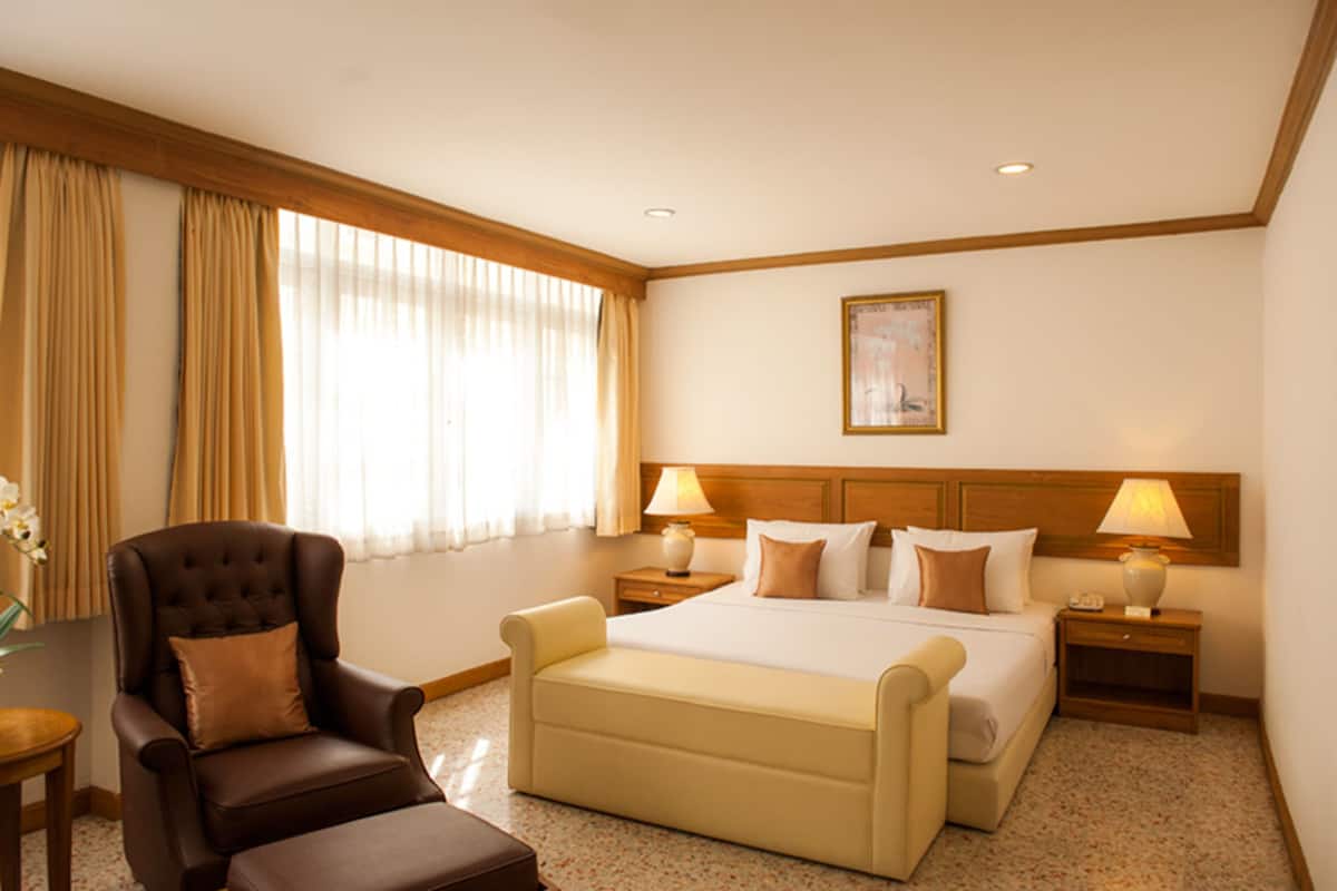 Une chambre d’hôtel avec un grand lit, deux tables de chevet avec des lampes, une chaise et une fenêtre avec des rideaux.