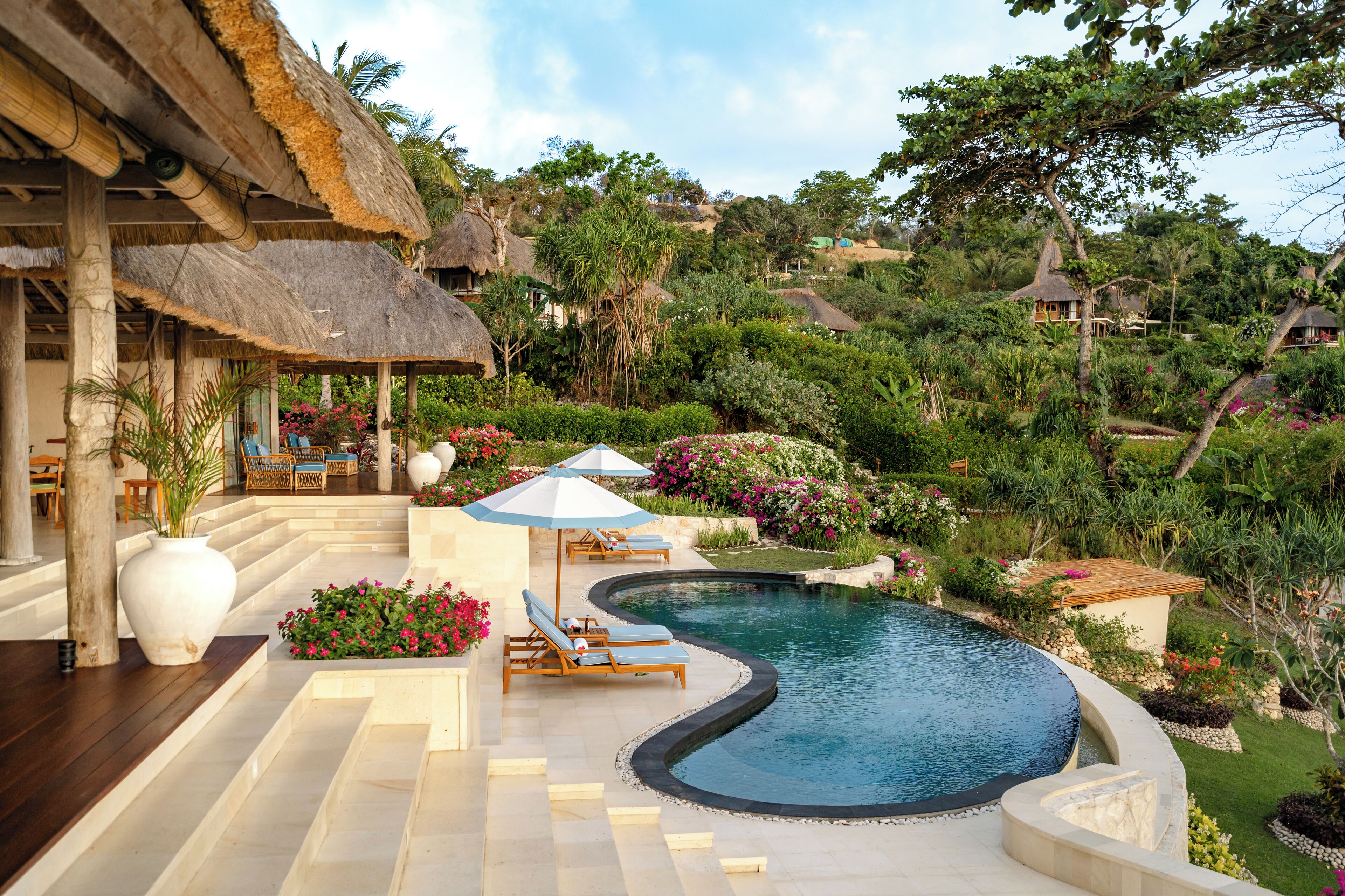 A pool area with lounge chairs, a thatched-roof structure, and lush greenery.