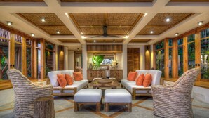 A spacious living area with wicker furniture, a ceiling fan, and large windows with tropical views. - NIHI Sumba - member Leading Hotels of the World (Wanokaka)
