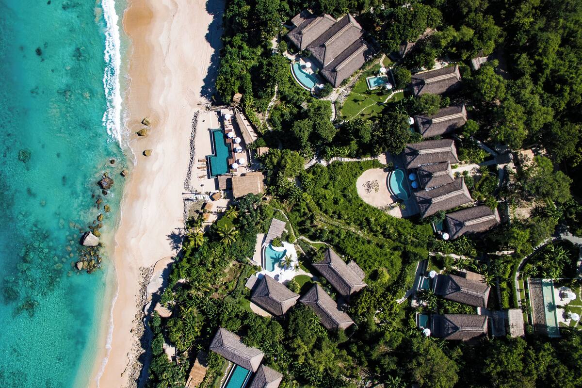 Vue aérienne d’un complexe hôtelier doté de plusieurs piscines, situé en bord de mer et entouré d’une végétation luxuriante.