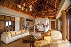A spacious living area with a high ceiling, a large sofa, a coffee table, and a bed with a canopy.