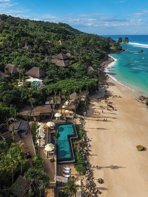 Un complejo turístico con piscina, playa y edificios de techo de paja.