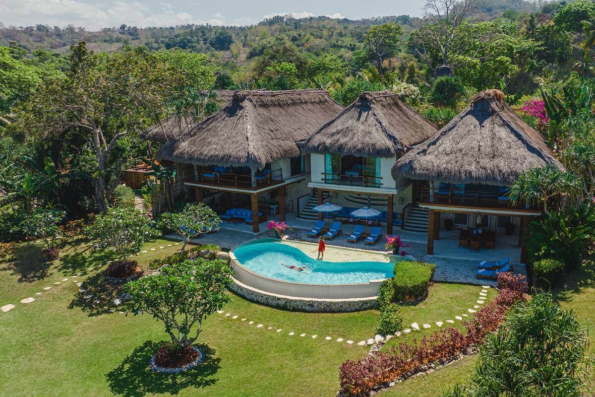 Un complexe hôtelier doté de villas aux toits de chaume, d’une piscine et de jardins luxuriants.