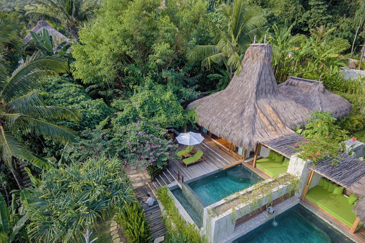 Un complexe hôtelier tropical doté d’une piscine, de bâtiments à toits de chaume et d’une végétation luxuriante.