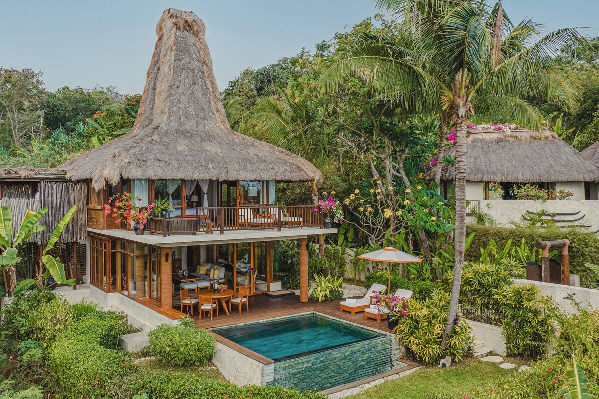 Une villa au toit de chaume, dotée d’une piscine et entourée d’une végétation luxuriante.