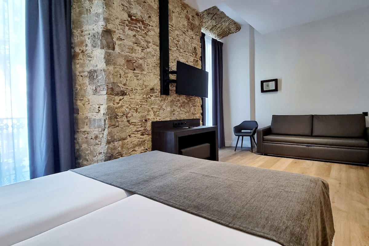 Una habitación de hotel moderna con una pared de acento de piedra, una cama, un sofá, un escritorio y una silla.