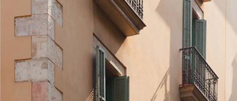 A building facade with multiple balconies, each with a metal railing and green shutters.