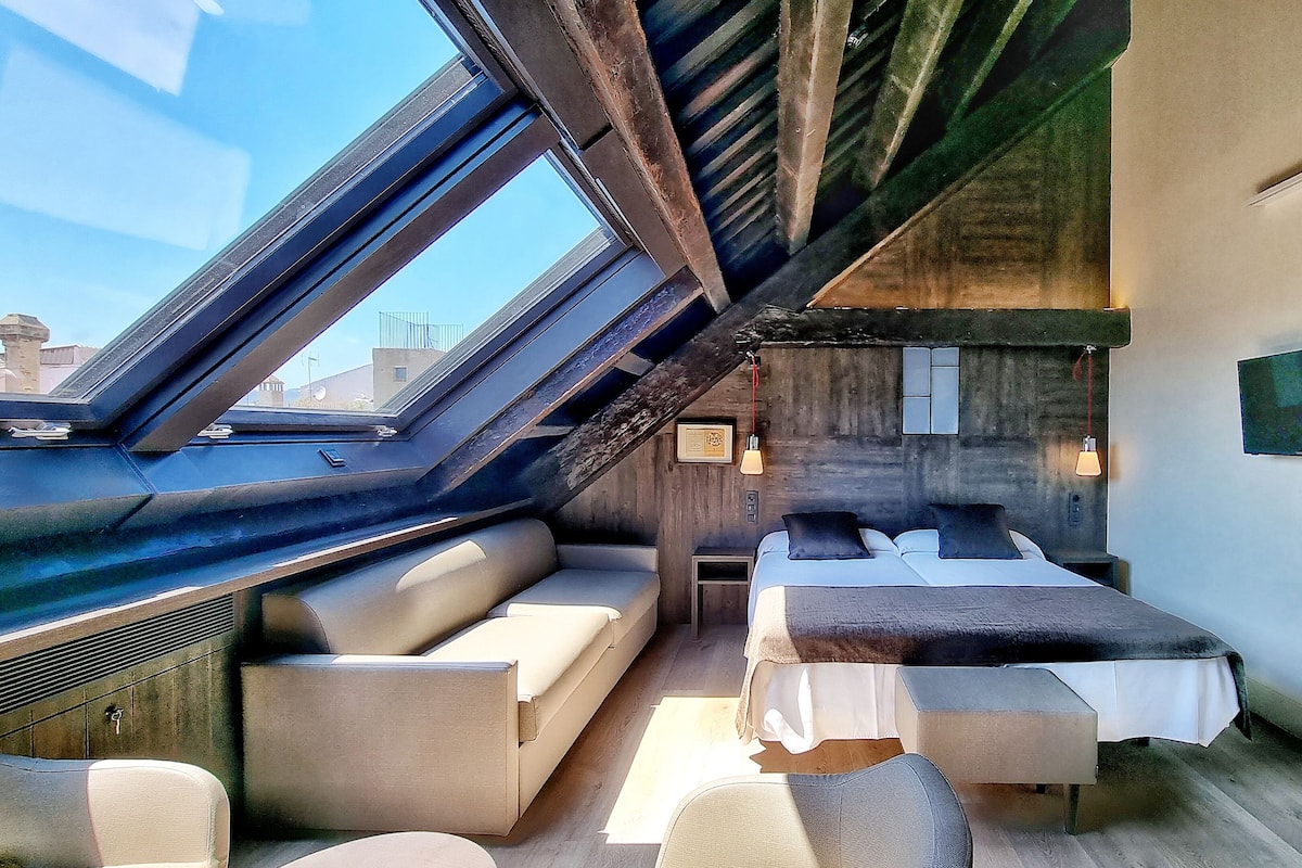 Una habitación compacta y moderna con tragaluz, cama y zona de estar.
