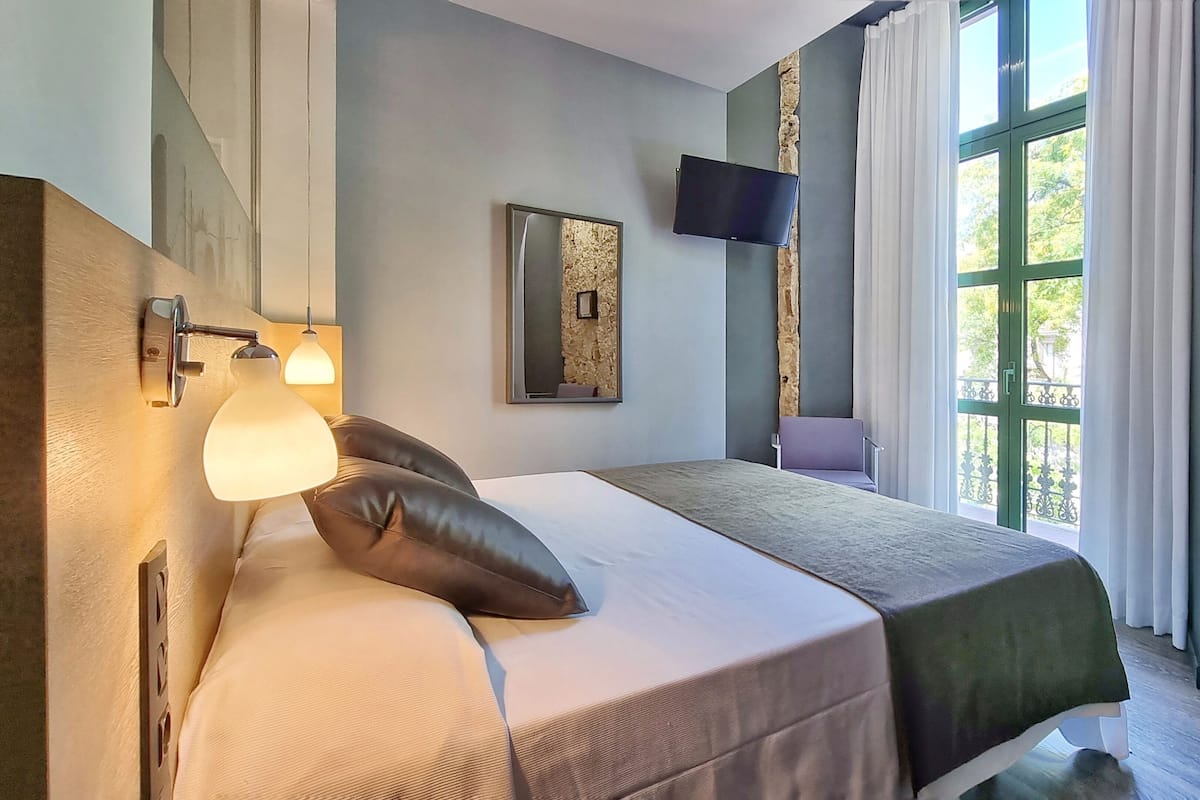 Un dormitorio moderno con cama, televisor montado y pared de piedra.