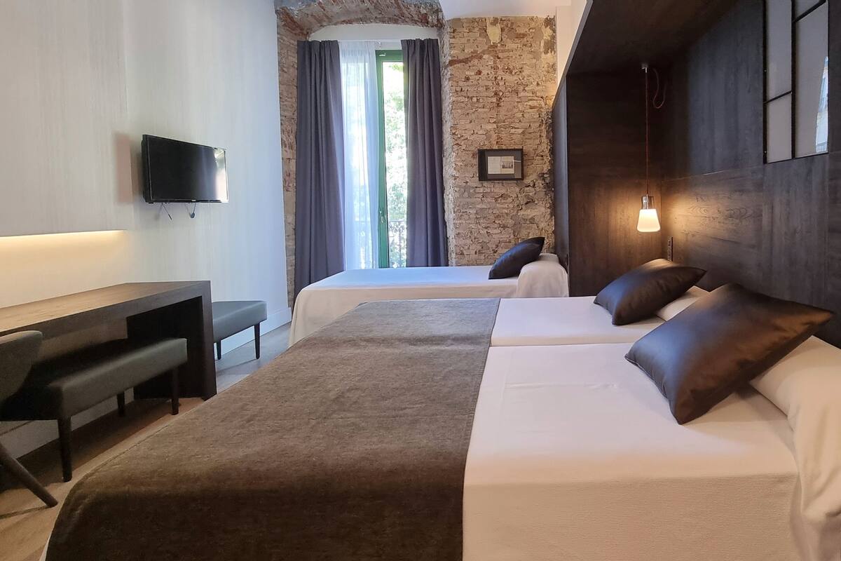 Habitación de hotel con dos camas, un escritorio, un televisor y una pared de piedra.