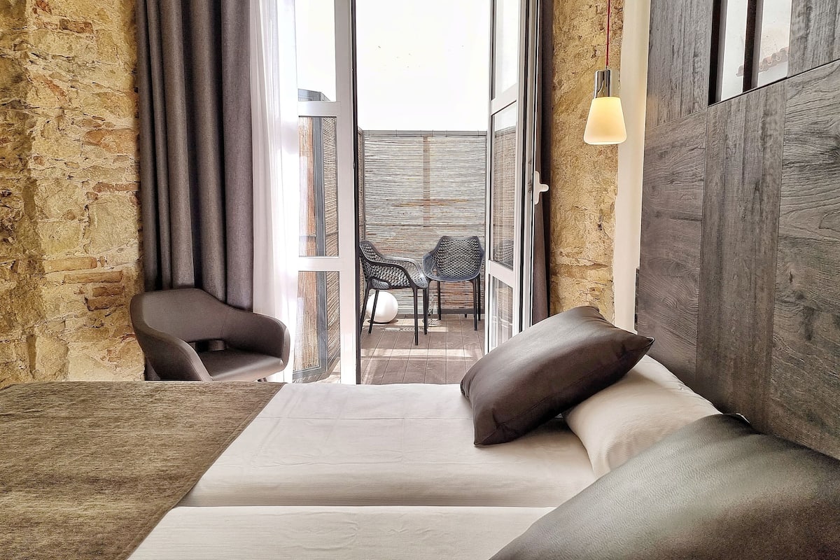 Habitación de hotel moderna con sofá cama, una mesita y vista al exterior a través de un ventanal.